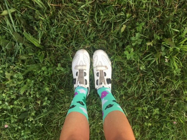 Legs of a woman wearing cycling shoes and colorful socks on grass