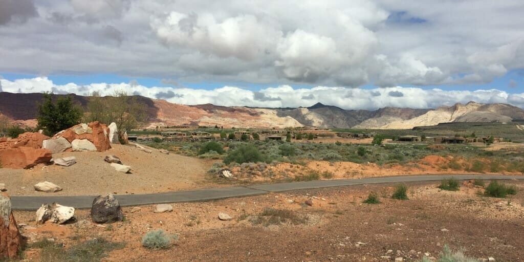 Narrow road in the middle of desert with mountains and big clouds